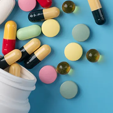 Pills and capsules are falling out of a white cup on a blue background